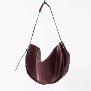 Gros plan détaillé du sac porté épaule demi-lune en cuir rouge foncé avec œillets métalliques.