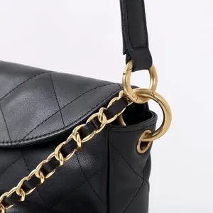 Vue rapprochée détaillée d'un sac bandoulière en cuir matelassé noir avec détails dorés.