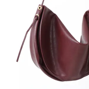 Détail de sac croissant en cuir bordeaux montrant la forme incurvée et œillets en métal.