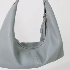 Vue détail de sac porté épaule en cuir souple, texture de sac croissant minimaliste et zip.