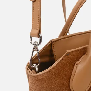 Gros plan de la bandoulière en cuir marron, fermoir métallique et texture de couture fine.