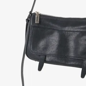 Gros plan détaillé d'un sac à bandoulière en cuir noir avec rabat vintage et quincaillerie.