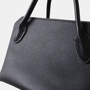 Gros plan sur le sac à main en cuir noir avec texture grainée et poignées doubles élégantes.