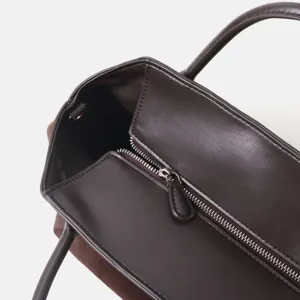 Détail élégant de sac cabas en cuir marron foncé avec fermeture zippée et poignées robustes.