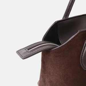 Gros plan détaillé de la tirette de fermeture éclair et de l'ouverture d'un sac en daim marron.