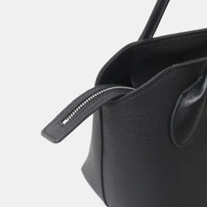Vue détaillée de sac à main en cuir noir, texture de vachette grainée premium avec fermeture éclair.