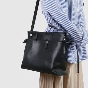 Détail de sac à bandoulière en cuir noir souple, nœuds latéraux et boutons.