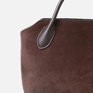 Gros plan détaillé d'un sac à main en daim marron avec une fixation précise de poignée en cuir.