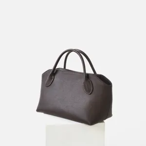 Gros plan du sac à main en cuir marron foncé, soulignant la texture fine et les poignées.