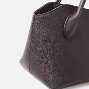 Détail de sac à main en cuir marron foncé montrant une texture grainée et une poignée.