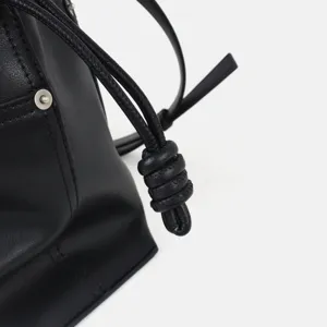 Gros plan sur un sac en cuir noir montrant le détail du nœud et du bouton métallique.