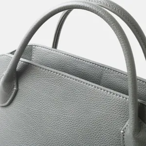 Gros plan des poignées de sac à main en cuir gris, texture premium et belles coutures.