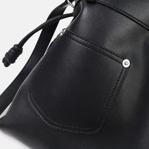 Détail du sac hobo en cuir souple noir avec une poche avant et une bandoulière nouée.