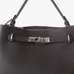 Gros plan sur les ferrures du sac en cuir marron foncé, texture grainée et fermoir en métal.