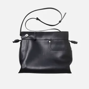 Gros plan détail du sac à épaule en cuir noir avec nœuds latéraux et bouton-pression.