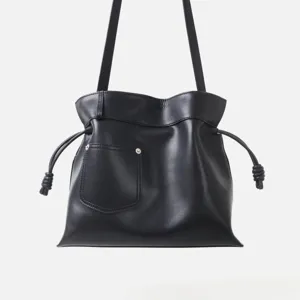 Détail de sac hobo noir en cuir souple avec cordon noué élégant et poche avant.