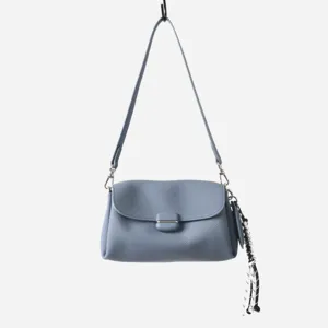 Bolso de hombro de cuero suave azul grisáceo, detalle de textura fina y borla decorativa.