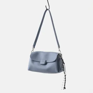 Detalle bolso de hombro de cuero azul, piel suave, hebilla de metal y elegante colgante lateral.
