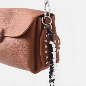 Detalle de bolso de cuero marrón con textura granulada herrajes y colgante de corazón.