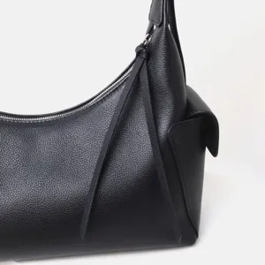 Detalle de bolso de hombro negro en cuero vacuno con bolsillo lateral y cremallera metálica.