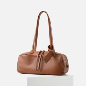 Primer plano del bolso de hombro tipo bolos de cuero marrón con textura suave y cremallera.