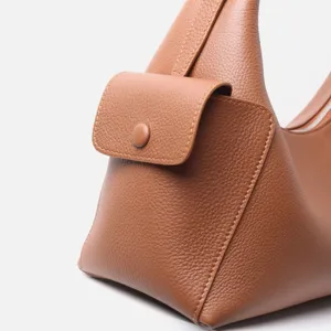 Primer plano detalle de bolso de hombro de cuero marrón con textura granulada y bolsillo.