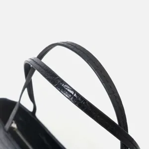 Close-up detail of black crocodile embossed leather handbag handle with fine stitching.