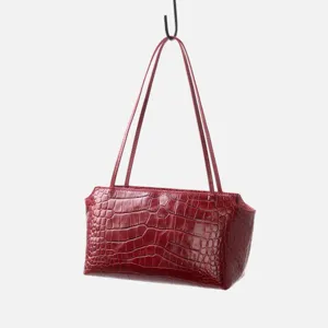 Detail view of the red crocodile embossed leather shoulder bag hanging on display.