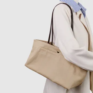 Vista detallada del bolso tote de lona beige con correa de cuero marrón y botón a presión.