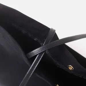 Primer plano detallado de bolso hobo de tela negra con correa de piel y herrajes dorados.