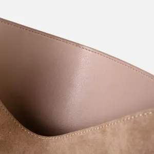 Primo piano della texture in pelle di vacchetta pregiata e delle cuciture di una borsa minimalista.