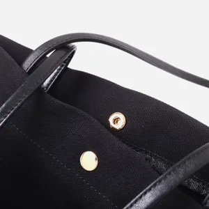 Primer plano detalle de bolso tote de tela negra con correa de cuero y botón magnético dorado.