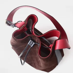 Bolso cubo de ante marrón con interior rojo, patrón acolchado y cordón ajustable.