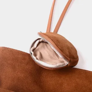 Primer plano del bolso tote de ante marrón con pequeño bolsillo con cremallera y tiras finas.