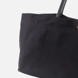 Vista detallada del bolso tote de lona negra, asa de cuero, bolso de mano commuter premium.
