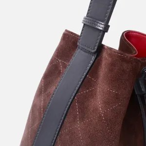 Detalle de bolso saco acolchado de ante marrón, correa de cuero negro, forro interior rojo.