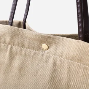 Detalle de bolso tote de lona con asas de cuero y botón a presión para uso diario.