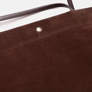 Detalle de bolso tote de ante marrón con textura fina, correa de cuero y botón de metal.