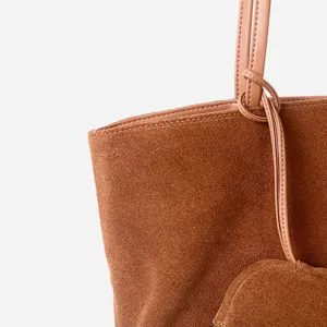 Vista detallada del asa y la textura del bolso tote de ante marrón con excelente acabado.