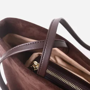 Detalle de bolso tote de ante marrón con asas de cuero premium y cierre de cremallera.