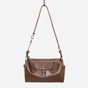 Detalle de bolso de cuero marron, correa ajustable, hebilla metalica y cierre de cremallera.