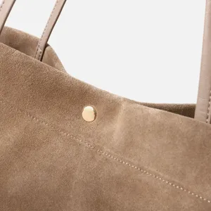 Detalle de bolso tote de ante marrón, diseño minimalista con asas finas y broche.