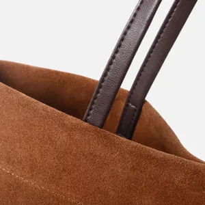 Detalle del asa del bolso tote de ante marrón con correa de cuero fina y textura suave.