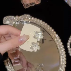 Nahaufnahme der glitzernden Kristall-Blumenohrringe auf einem eleganten Perlenspiegel.
