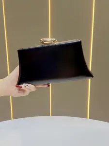 Close-up detail of an elegant black evening clutch bag with gold metallic clasp in hand.