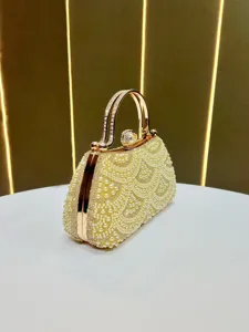 Close-up detail of luxury gold evening clutch with pearl and rhinestone geometric patterns.