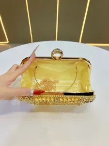 Elegante bolso de noche dorado con pedrería, correa de cadena y cierre de cristal.