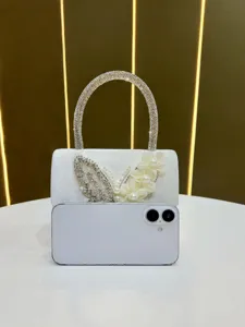 Elegant white evening bag detail with rhinestone handle and butterfly decor.