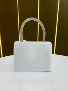 Close up detail of elegant white evening bag featuring sparkling rhinestone handle.