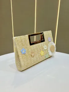 Straw woven clutch bag detail with metallic handle and colorful crochet floral decorations.